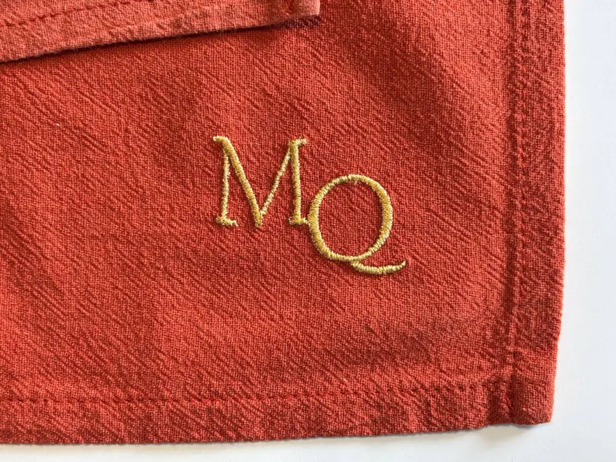 Monogramme MQ brodé en fil doré sur une serviette rouge brique